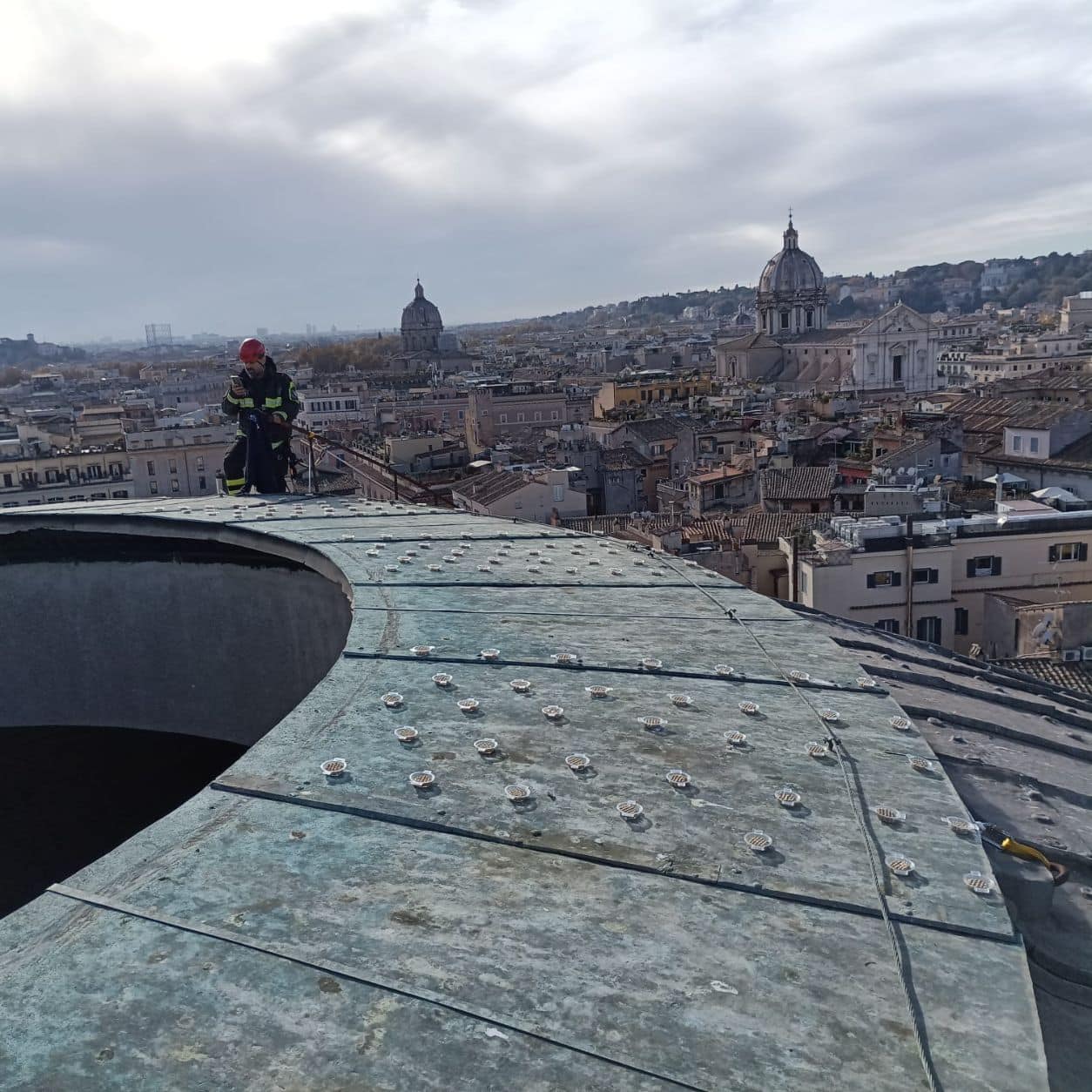 Tecnico in imbracatura al lavoro sulla cupola del Pantheon, con i tetti di Roma sullo sfondo