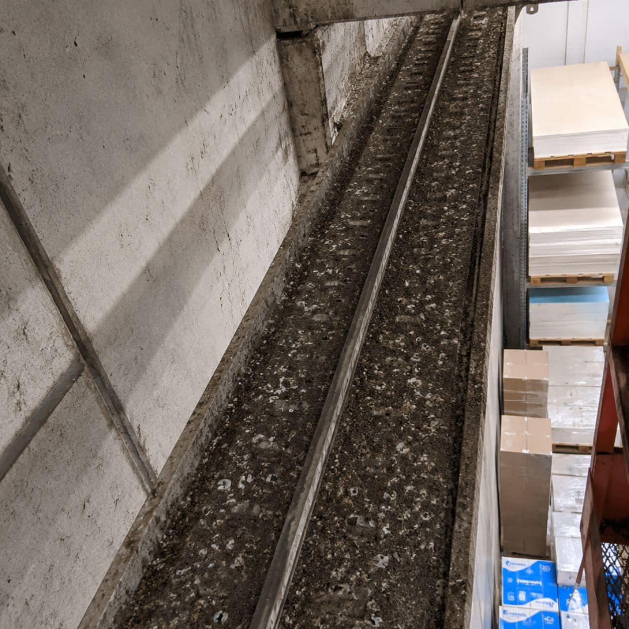 Trave in cemento sotto la copertura di un magazzino, segnata da colate di guano, con bancali di merce impilati sotto