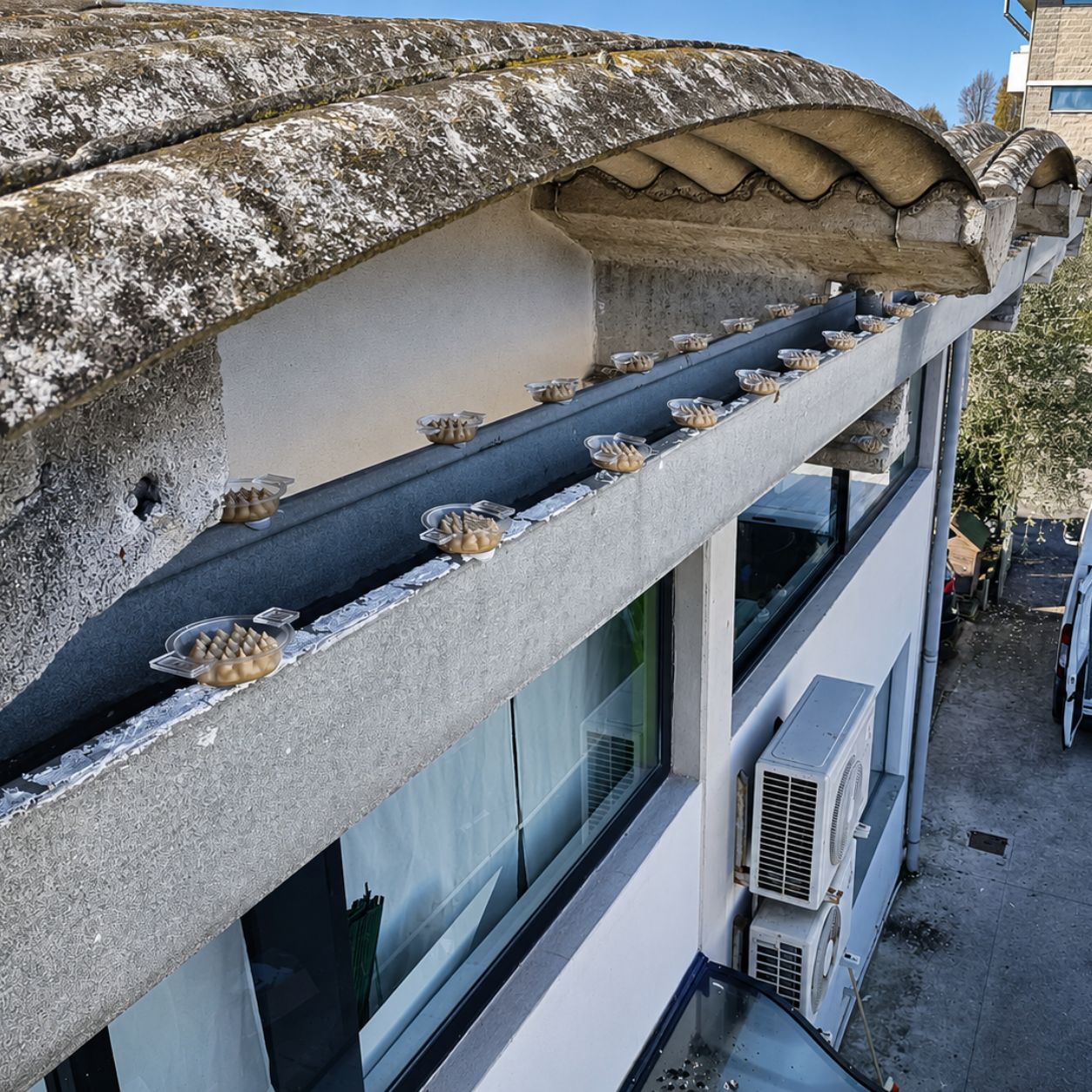 Gronda di un edificio trattata con dissuasori, e sotto il terrazzo con due unità esterne di climatizzazione