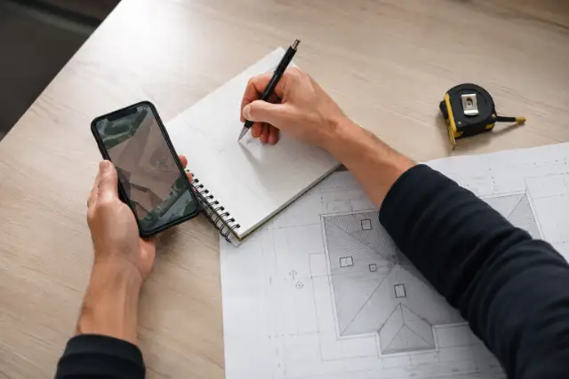 Tecnico che prende appunti al telefono con la planimetria di un tetto sulla scrivania