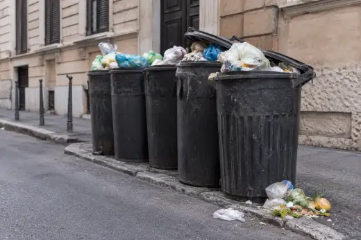 Cassonetti dei rifiuti scoperti e residui alimentari in una via cittadina italiana