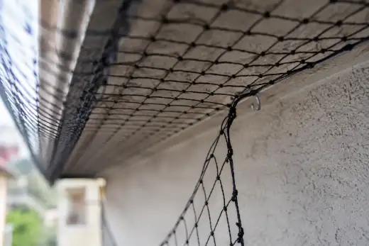 Rete anti-volatili sganciata dal cavo di bordo che pende allentata, con un varco aperto fra la rete e il muro