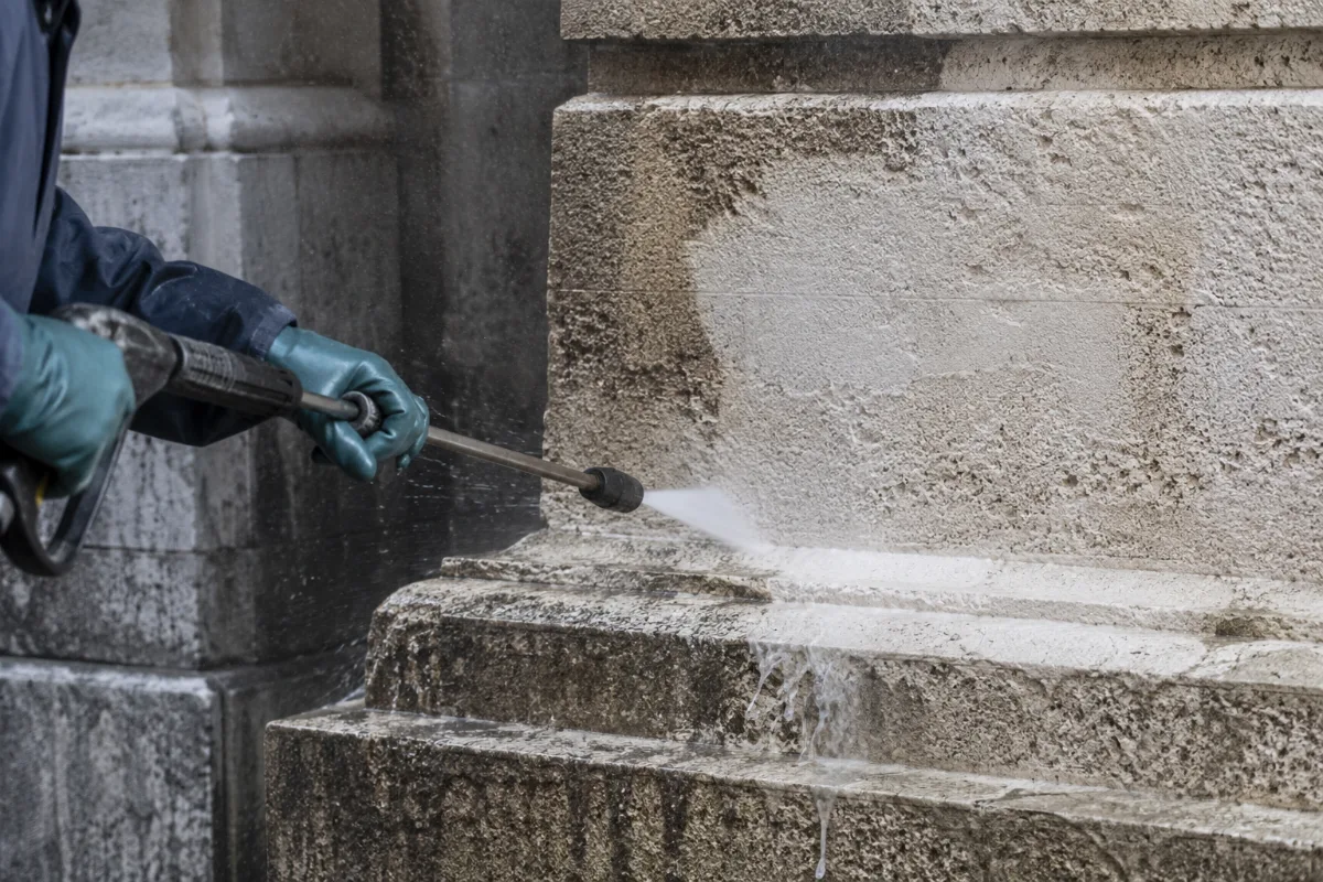 Getto di idropulitrice ad alta pressione diretto contro una superficie in pietra storica, con acqua che rimbalza sul paramento