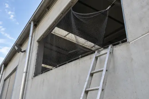 Rete anti volatili nera allentata sul bordo di un’apertura di capannone, con una scala a pioli appoggiata alla parete