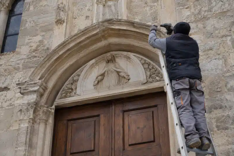 Operatore su una scala che fissa un filo sopra il portale in pietra di una chiesa