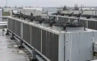 Una decina di piccioni posati sui telai e sulle griglie dei ventilatori di due file di dry cooler, con colature di guano sui pannelli laterali