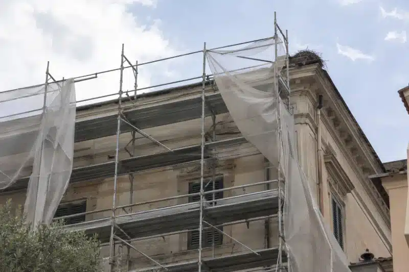 Ponteggio fermo con i teli su una facciata storica, con un nido sulla cornice del tetto