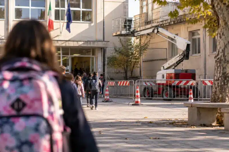 Studenti che entrano a scuola accanto a un cantiere recintato con piattaforma aerea davanti all'ingresso