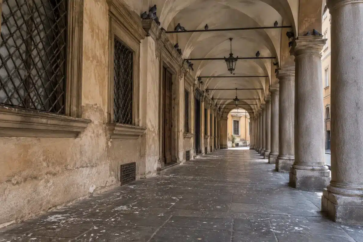 Sottoportico di un centro storico con la pavimentazione in pietra punteggiata di guano e alcuni piccioni posati sui cornicioni delle volte