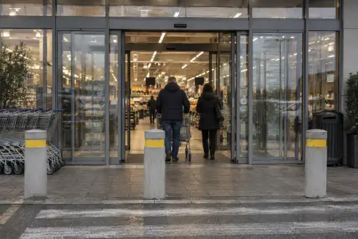 Porte automatiche scorrevoli di un supermercato aperte, con clienti che entrano e carrelli