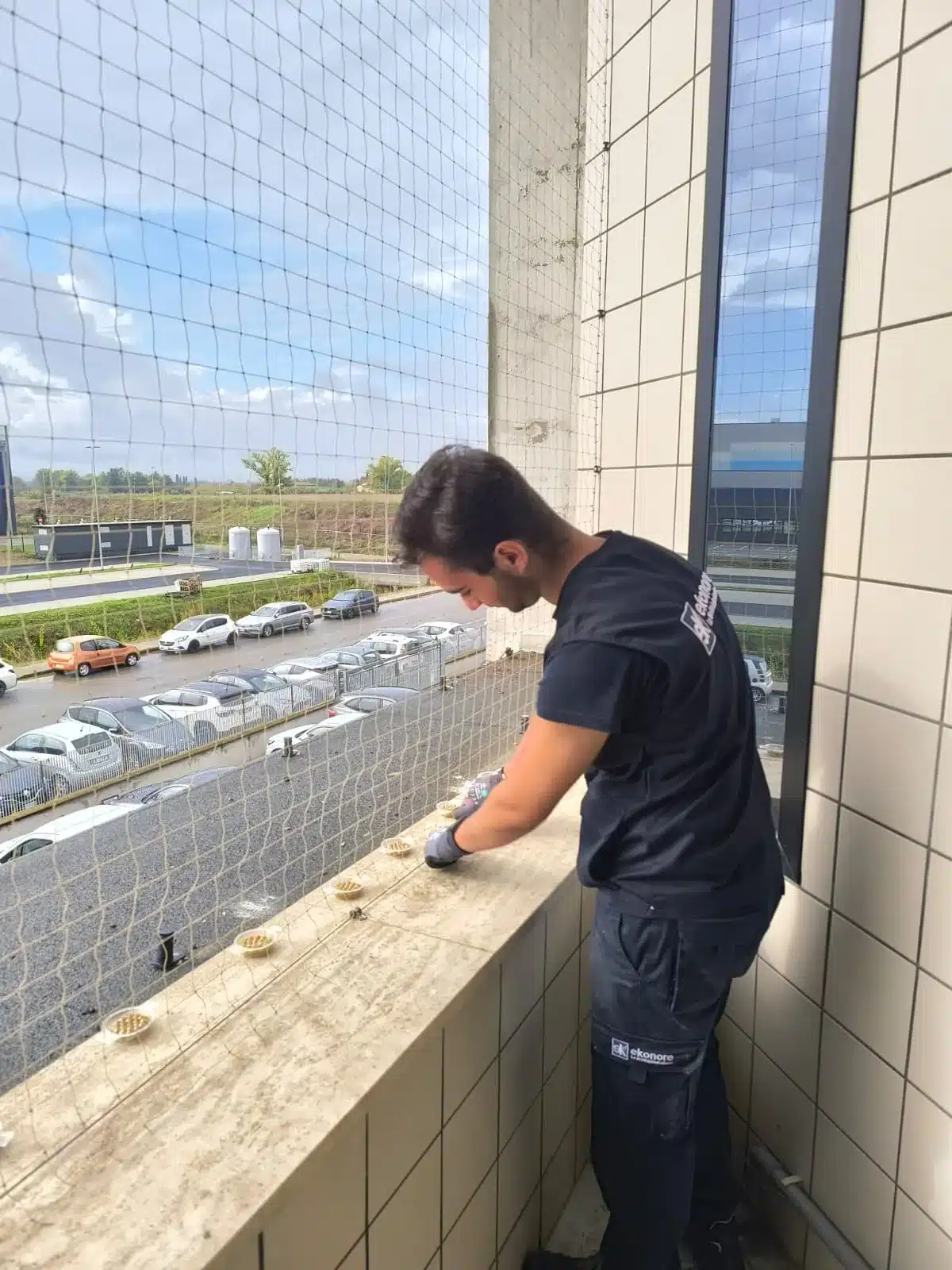 Tecnico Ekonore posa le coppette BirdFire sul parapetto di una loggia chiusa con la rete